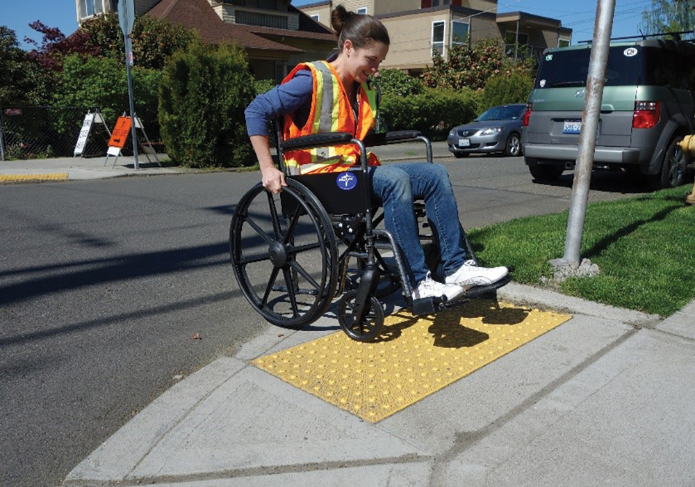 A lady in a wheelchair is getting on a curb ramp.