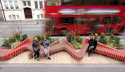 People sitting on a bench in front of a red bus